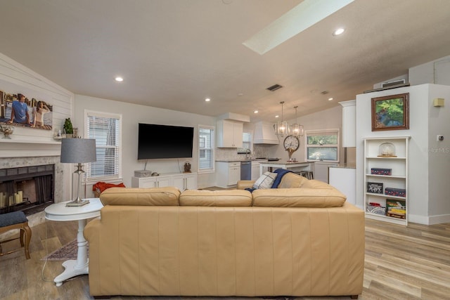 living room featuring lofted ceiling with skylight, light wood-style flooring, a fireplace, and an inviting chandelier