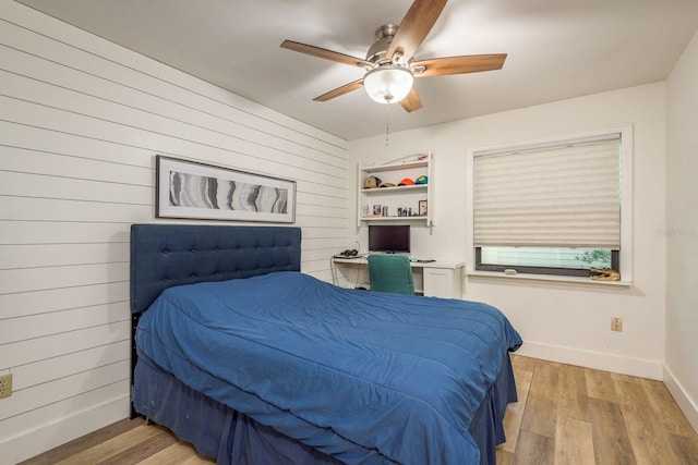 bedroom featuring light wood finished floors, wooden walls, ceiling fan, and baseboards