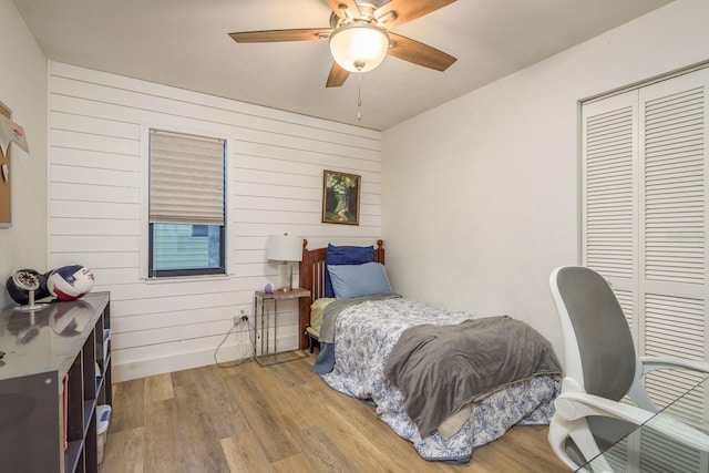 bedroom featuring ceiling fan, a closet, wood finished floors, and wood walls