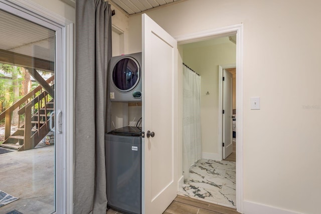 laundry area featuring laundry area, baseboards, stacked washer / drying machine, and marble finish floor