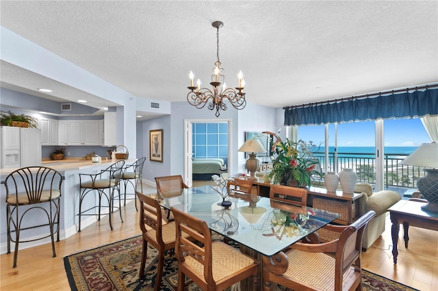 dining room featuring light wood-type flooring, visible vents, a water view, a textured ceiling, and a chandelier