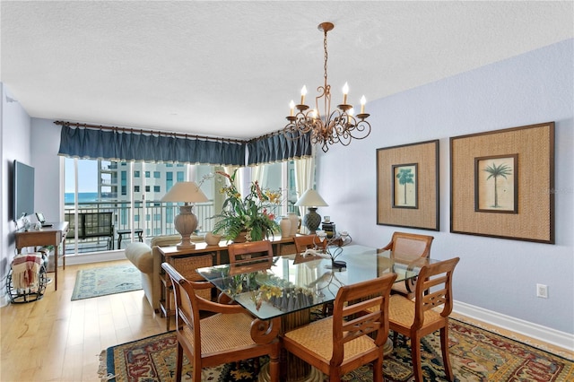 dining space featuring baseboards, a notable chandelier, wood finished floors, and a textured ceiling