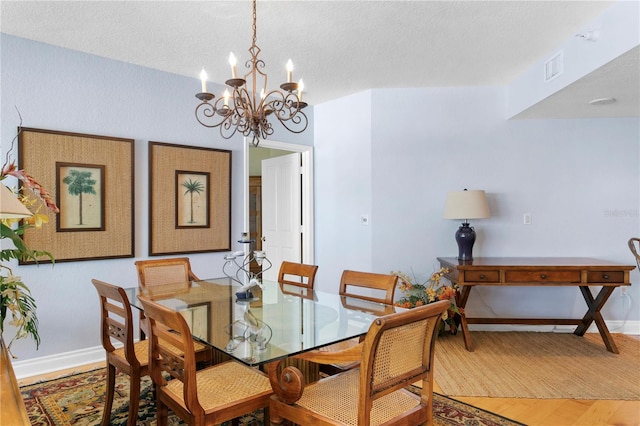 dining space featuring visible vents, baseboards, wood finished floors, a notable chandelier, and a textured ceiling