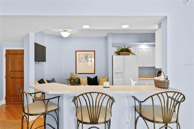 kitchen with light countertops, a kitchen breakfast bar, recessed lighting, and light wood-type flooring