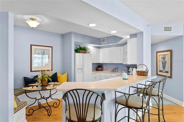 kitchen with light wood-type flooring, visible vents, a breakfast bar, and a peninsula