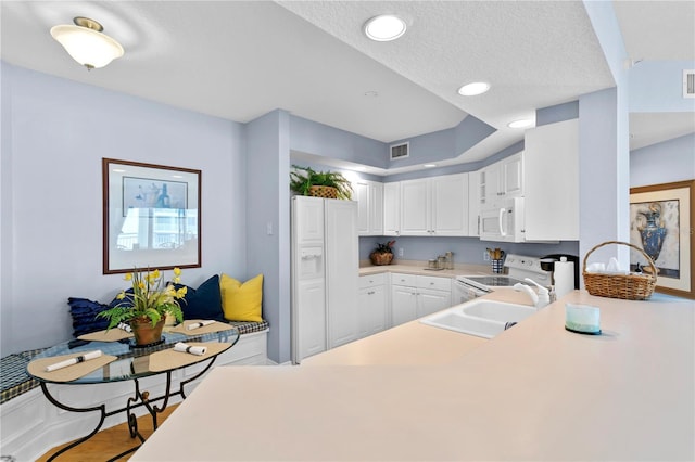 kitchen featuring visible vents, a sink, white cabinetry, white appliances, and light countertops