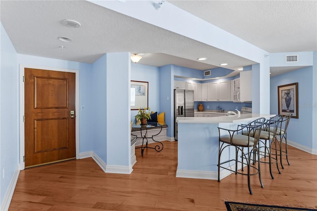 kitchen featuring a peninsula, light wood-style floors, stainless steel fridge with ice dispenser, baseboards, and a textured ceiling