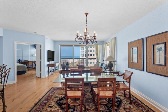 dining area with a textured ceiling, a chandelier, baseboards, and light wood-style floors