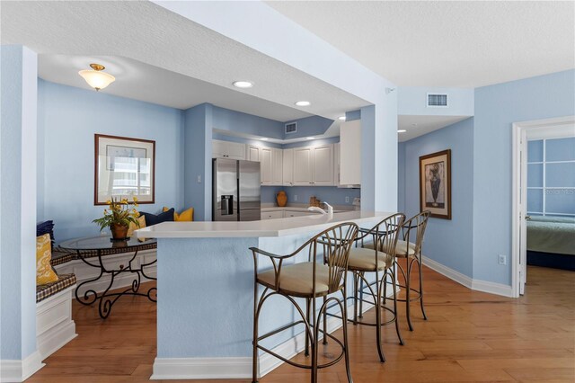 kitchen with light wood-style floors, baseboards, visible vents, stainless steel refrigerator with ice dispenser, and a peninsula