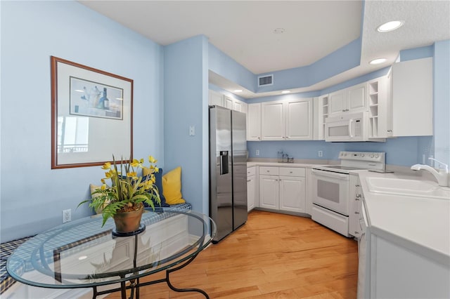 kitchen with white cabinets, a sink, visible vents, light wood finished floors, and white appliances