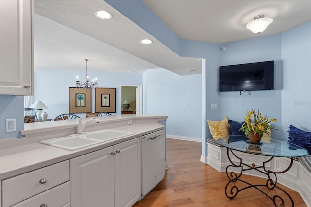 kitchen with white dishwasher, a sink, white cabinetry, a notable chandelier, and a peninsula