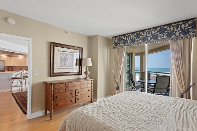 bedroom with a water view, access to exterior, light wood-style flooring, baseboards, and a textured ceiling