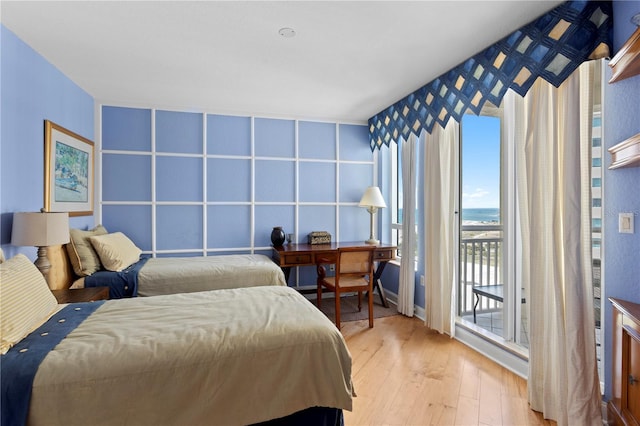 bedroom featuring baseboards, access to outside, a water view, and light wood-style flooring