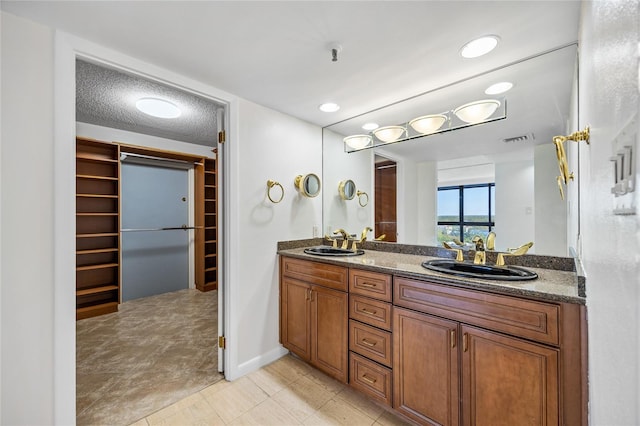 bathroom with double vanity, visible vents, a walk in closet, and a sink