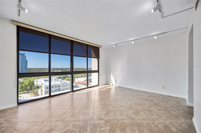 tiled spare room featuring a textured ceiling, rail lighting, baseboards, and expansive windows