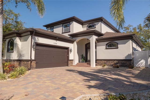 mediterranean / spanish-style house featuring stone siding, stucco siding, an attached garage, and driveway