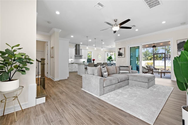 living area featuring light wood finished floors, visible vents, ceiling fan, and ornamental molding