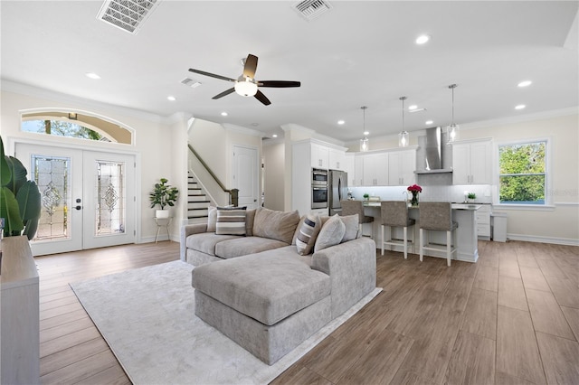 living area with visible vents, light wood-style flooring, stairs, and ornamental molding