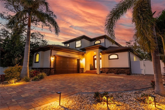 view of front of house with stucco siding, a garage, stone siding, driveway, and a gate