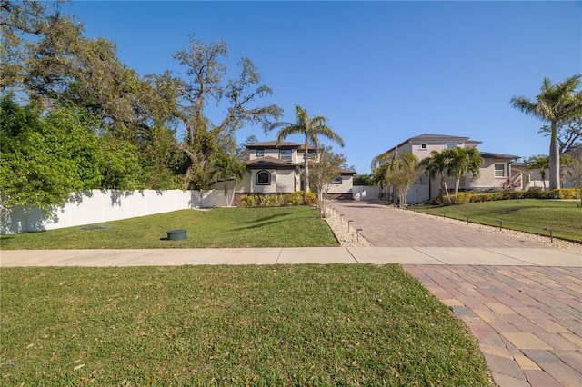 view of front of home featuring a front yard, decorative driveway, fence, and stucco siding