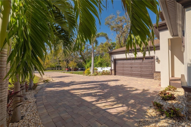 exterior space with stone siding, stucco siding, an attached garage, and decorative driveway