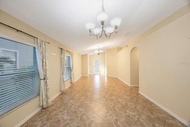 spare room featuring tile patterned floors, baseboards, arched walkways, and an inviting chandelier