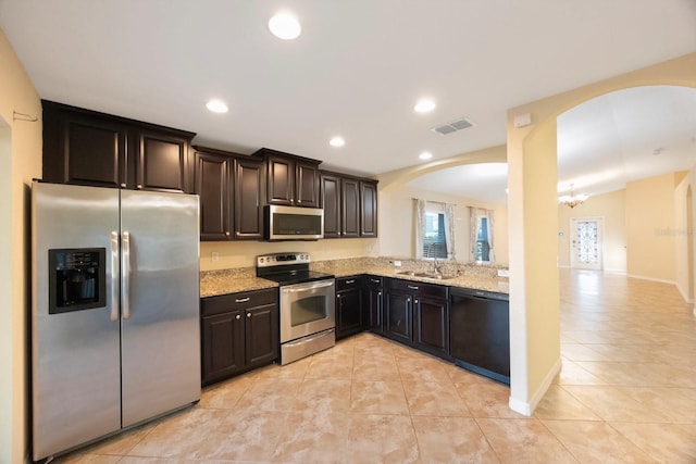 kitchen with visible vents, a sink, stainless steel appliances, arched walkways, and light stone countertops