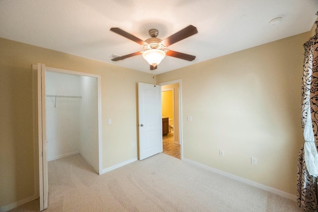 unfurnished bedroom with baseboards, ceiling fan, a closet, a walk in closet, and light colored carpet