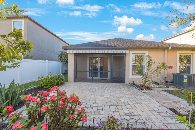 rear view of property featuring a sunroom, fence, central AC, and stucco siding