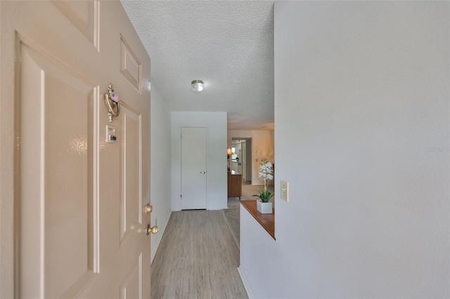 hall with a textured ceiling and light wood-style floors