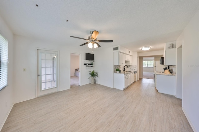 unfurnished living room featuring a sink, a textured ceiling, a ceiling fan, and light wood finished floors