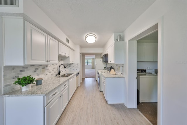 kitchen with visible vents, a sink, white gas range oven, black microwave, and washer and clothes dryer