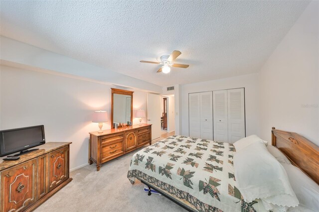 bedroom featuring visible vents, light colored carpet, a closet, a textured ceiling, and a ceiling fan