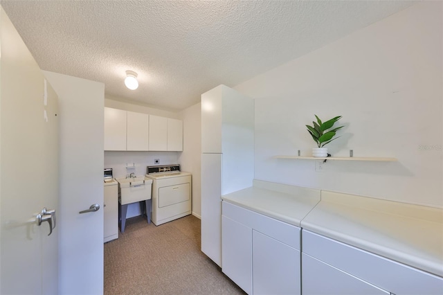 laundry area with a textured ceiling, washing machine and dryer, cabinet space, and light carpet