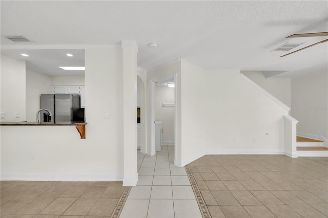 unfurnished living room featuring visible vents, a textured ceiling, light tile patterned flooring, baseboards, and stairs