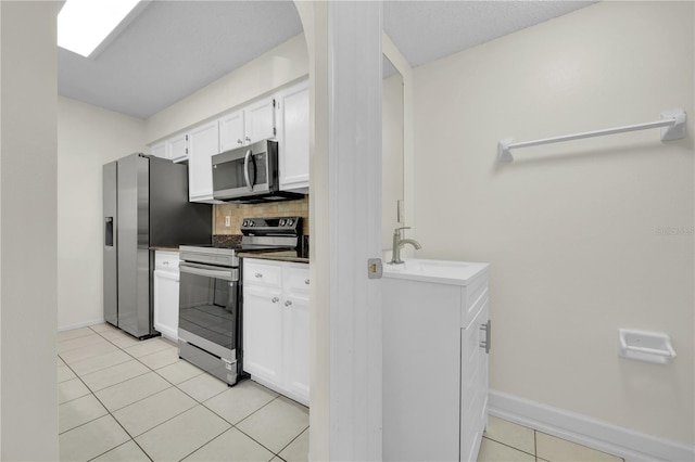 kitchen with a sink, white cabinetry, stainless steel appliances, light tile patterned floors, and baseboards