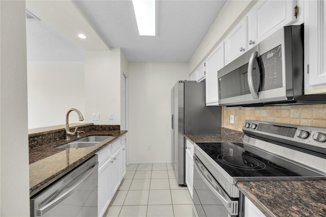 kitchen with dark stone counters, a sink, stainless steel appliances, white cabinets, and backsplash