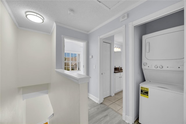 washroom with stacked washing maching and dryer, laundry area, light wood-style flooring, ornamental molding, and a textured ceiling