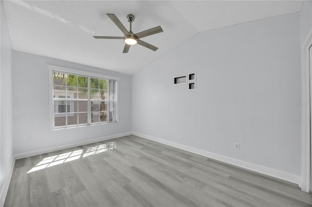 spare room with wood finished floors, baseboards, ceiling fan, vaulted ceiling, and a textured ceiling