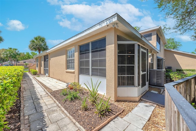 view of property exterior featuring central AC unit, stucco siding, fence, and a sunroom