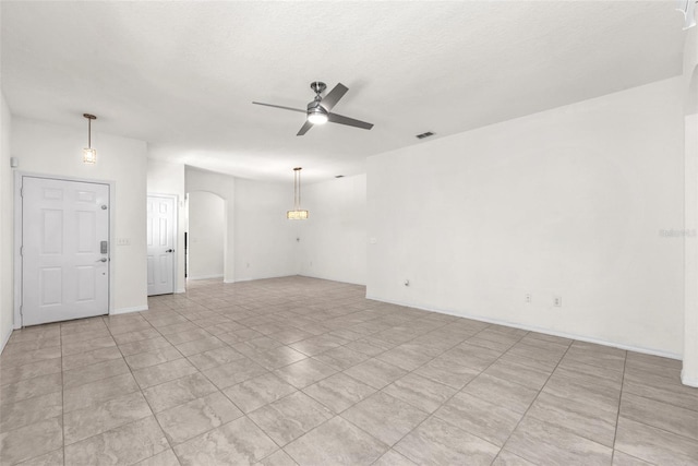 unfurnished room with visible vents, a ceiling fan, a textured ceiling, arched walkways, and baseboards