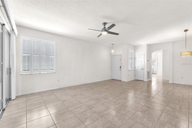 unfurnished living room featuring light tile patterned floors, a ceiling fan, baseboards, arched walkways, and a textured ceiling