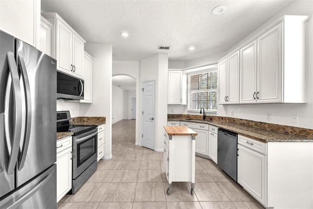 kitchen featuring wooden counters, arched walkways, a sink, white cabinets, and appliances with stainless steel finishes