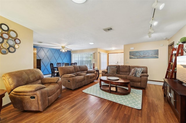 living area with visible vents, track lighting, wood finished floors, baseboards, and an accent wall