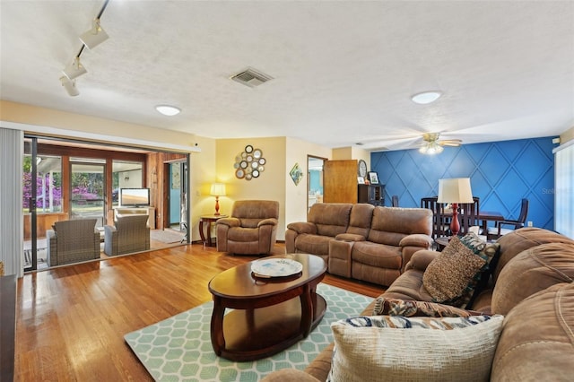 living room featuring a ceiling fan, wood finished floors, visible vents, a textured ceiling, and an accent wall