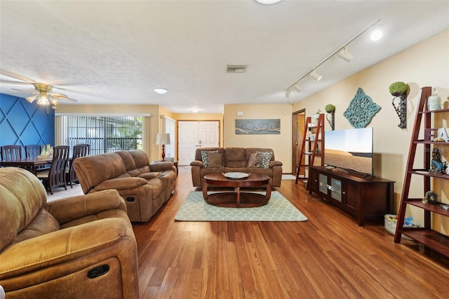 living area with visible vents, a textured ceiling, wood finished floors, rail lighting, and ceiling fan