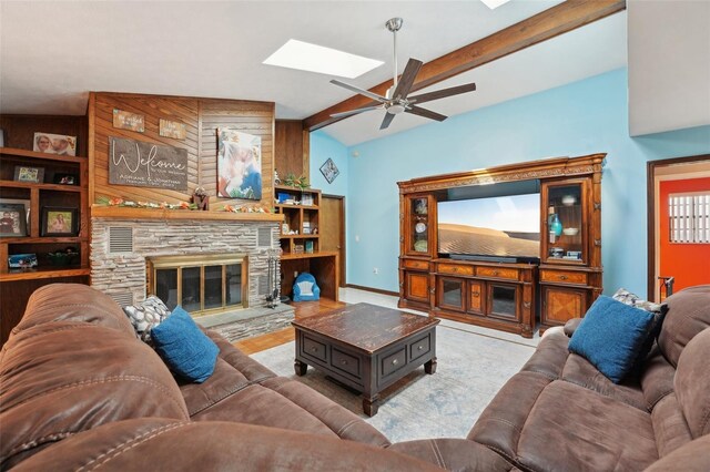 living area featuring baseboards, lofted ceiling with skylight, a stone fireplace, and a ceiling fan