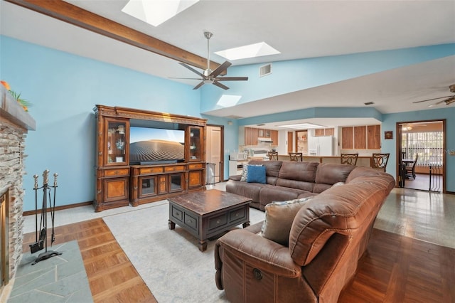 living area featuring visible vents, lofted ceiling with skylight, a stone fireplace, and a ceiling fan