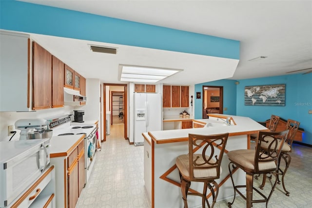 kitchen featuring visible vents, a kitchen bar, under cabinet range hood, white appliances, and light floors