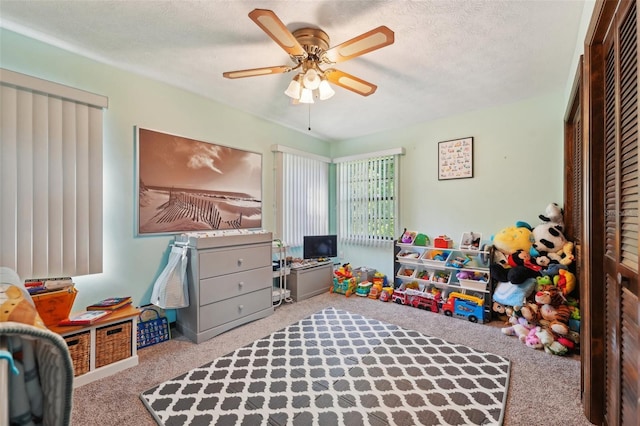 recreation room with a textured ceiling, ceiling fan, and carpet flooring